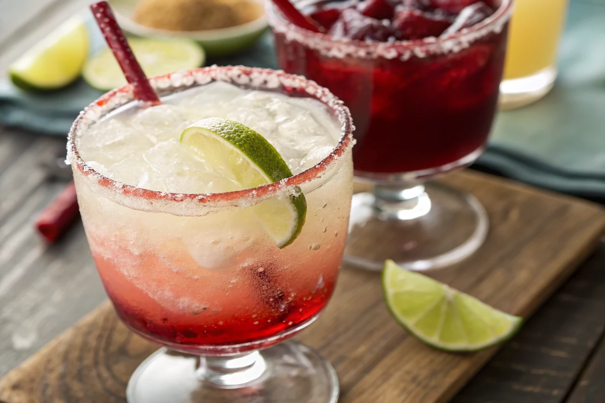 Close-up of red sangria streaking down into pale frozen margarita slush inside a clear glass with a chile lime rim