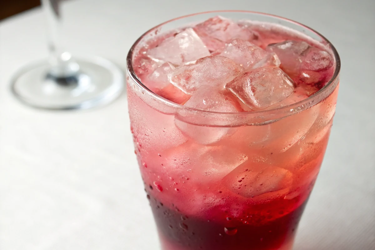 Close-up of a layered pink cocktail over ice showing the gradient from dark red at the base through coral to light pink at the rim