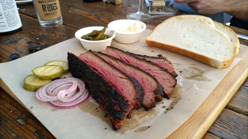 Close-up of a brisket flat showing pencil-thick slices, visible smoke ring under a peppery bark, and rendered fat