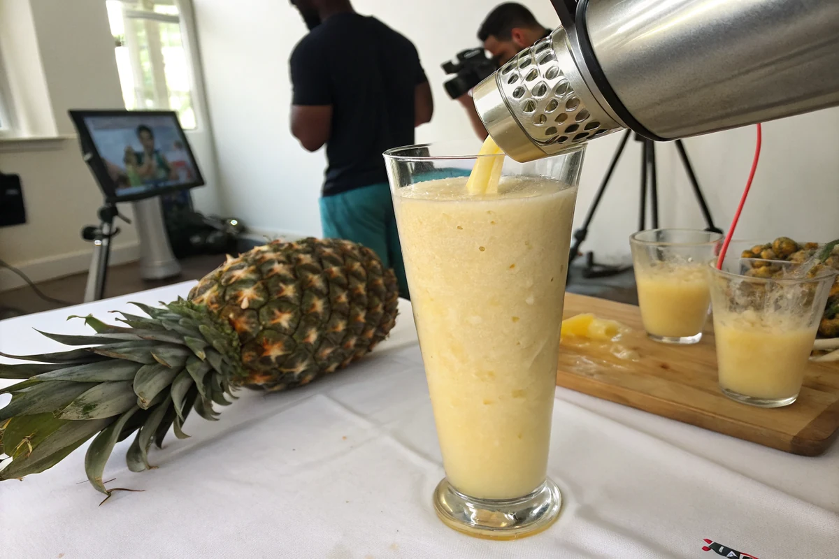 Close-up of a blended frozen tropical cocktail being poured from a blender into a tall glass, thick creamy pina colada texture with pineapple juice