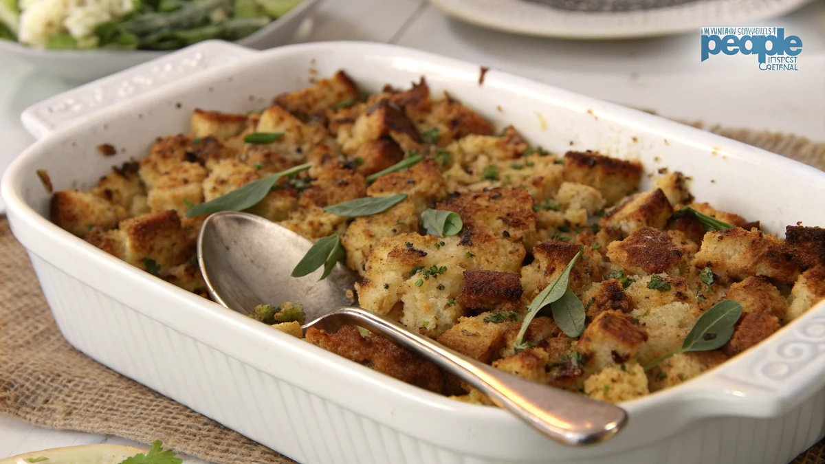 Golden Texas toast stuffing in a white 9 by 13 baking dish with a crisp browned top, flecks of fresh sage and parsley visible, a serving spoon resting in the corner