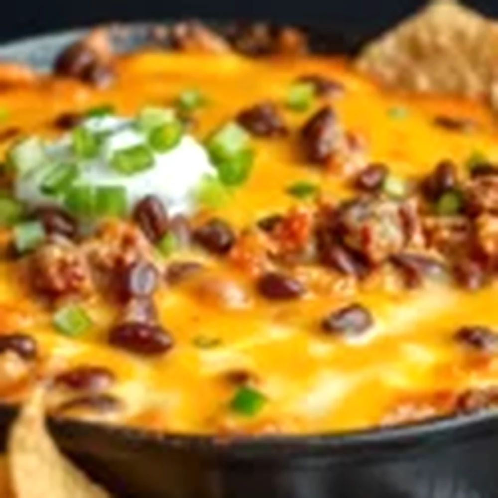 Overhead view of a 9x13 dish of Texas trash dip surrounded by tortilla chips, lime wedges, and a Mexican lager on a Texas patio table