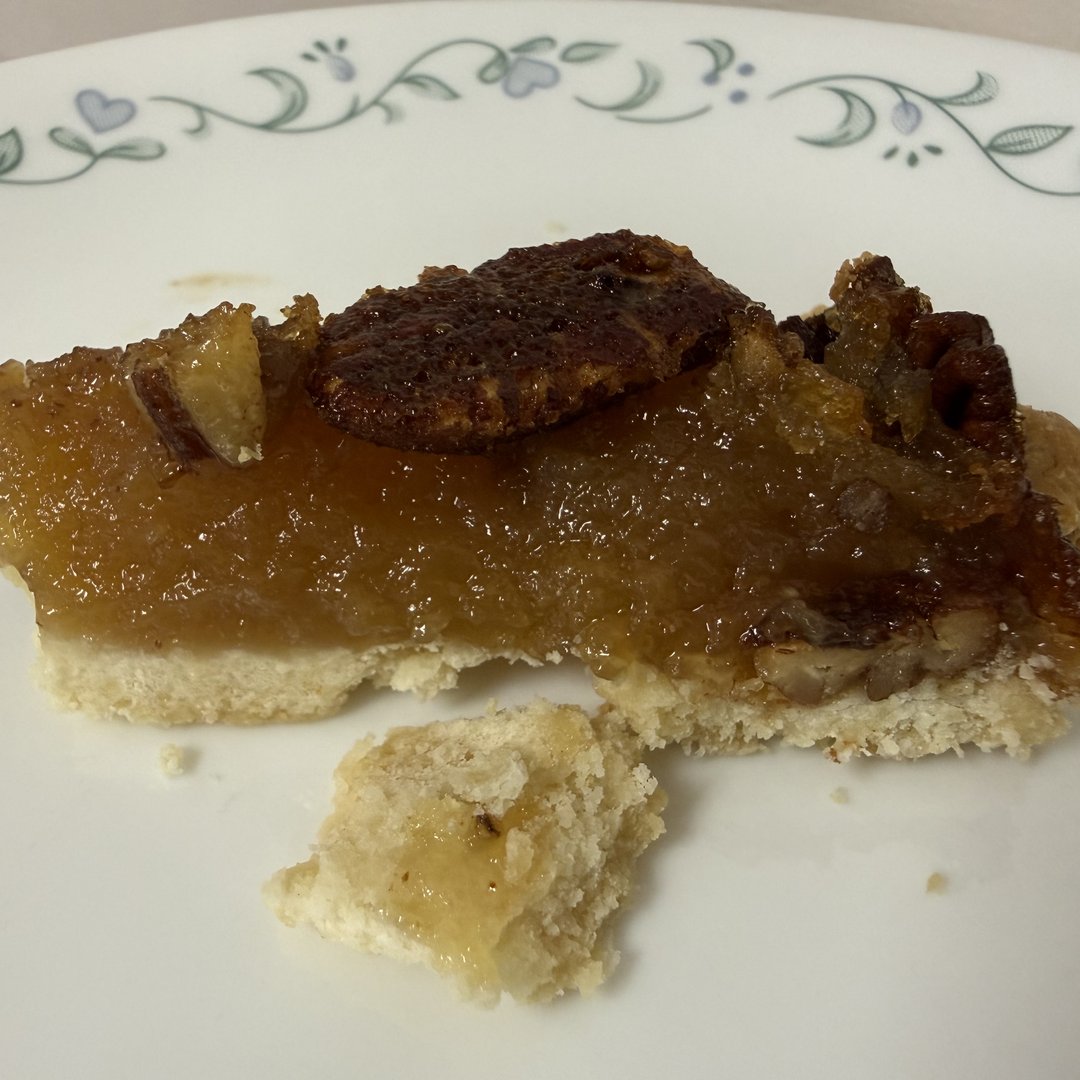 Close up slice of Texas pecan pie showing gooey caramel and pecan halves on a decorative plate