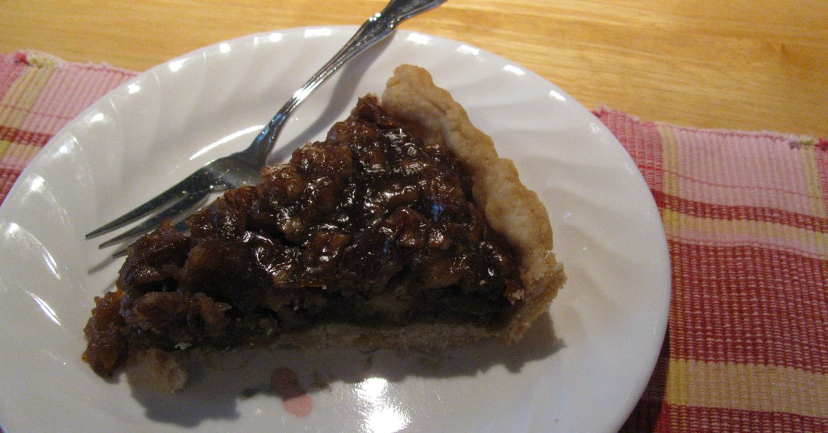 Slice of Texas pecan pie on a white plate with a fork showing the gooey dark filling
