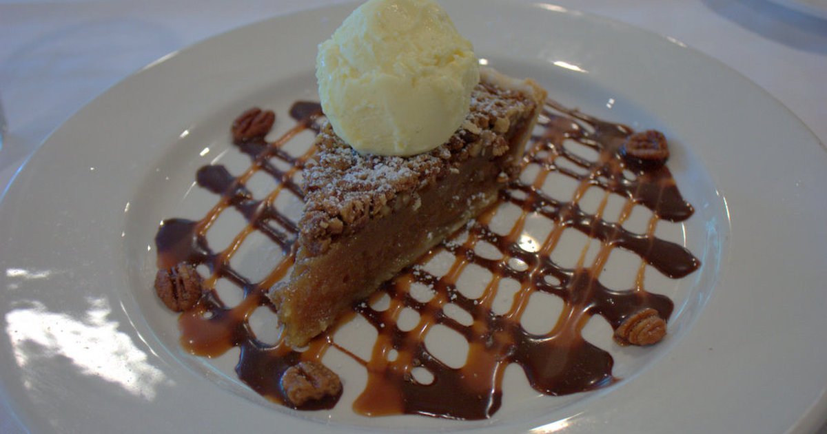 Slice of Texas pecan pie with vanilla ice cream and caramel drizzle on a white restaurant plate